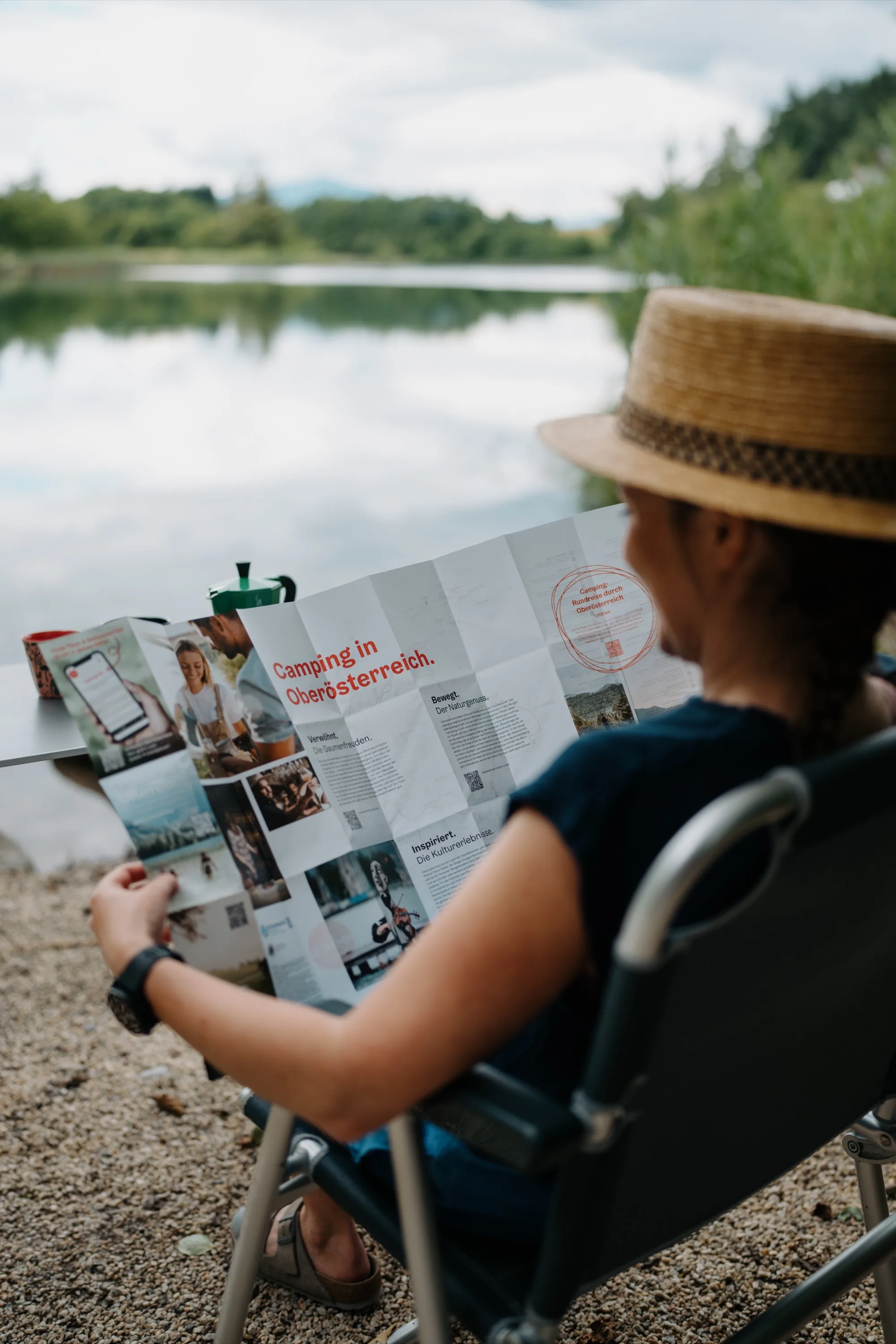 Campeggio nell'Alta Austria – donna con cappello di paglia legge una mappa pieghevole s-format in riva al lago