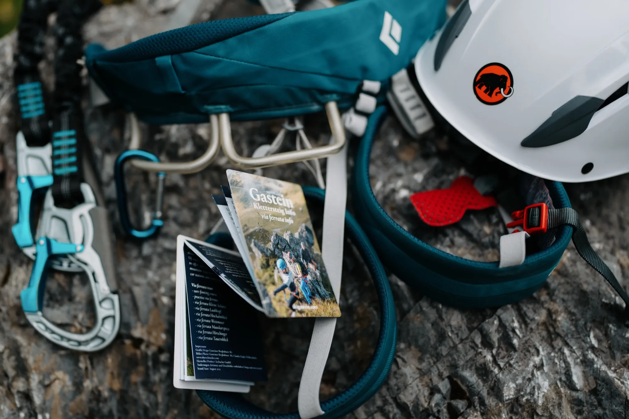 Guida per via ferrata Gasteinertal Twin-Card accanto all'attrezzatura da arrampicata – casco, moschettone e imbracatura sulla roccia