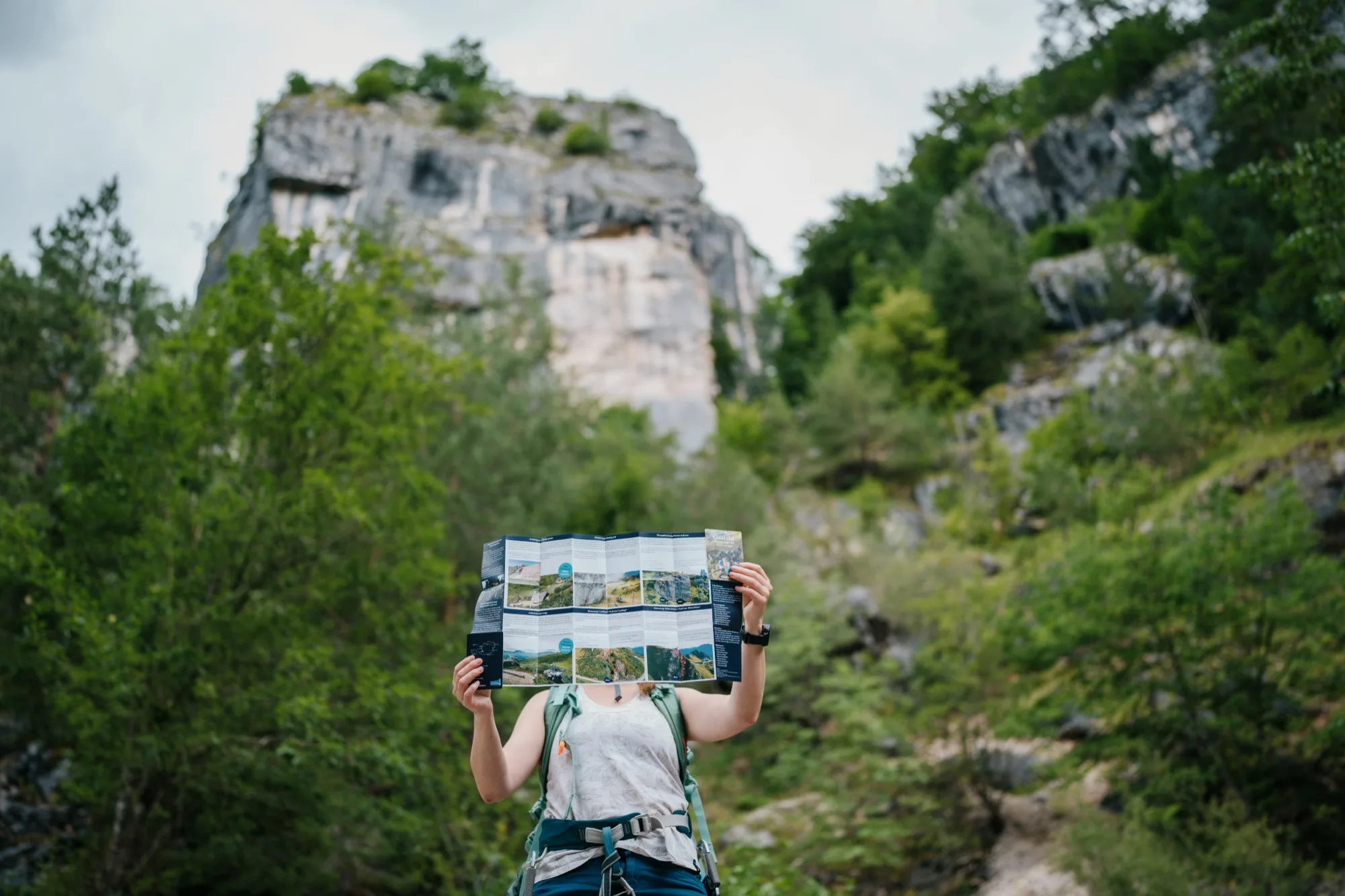 Arrampicatrice tiene aperta la guida delle vie ferrate della Gasteinertal davanti a un'imponente parete rocciosa – mappa pieghevole outdoor in uso