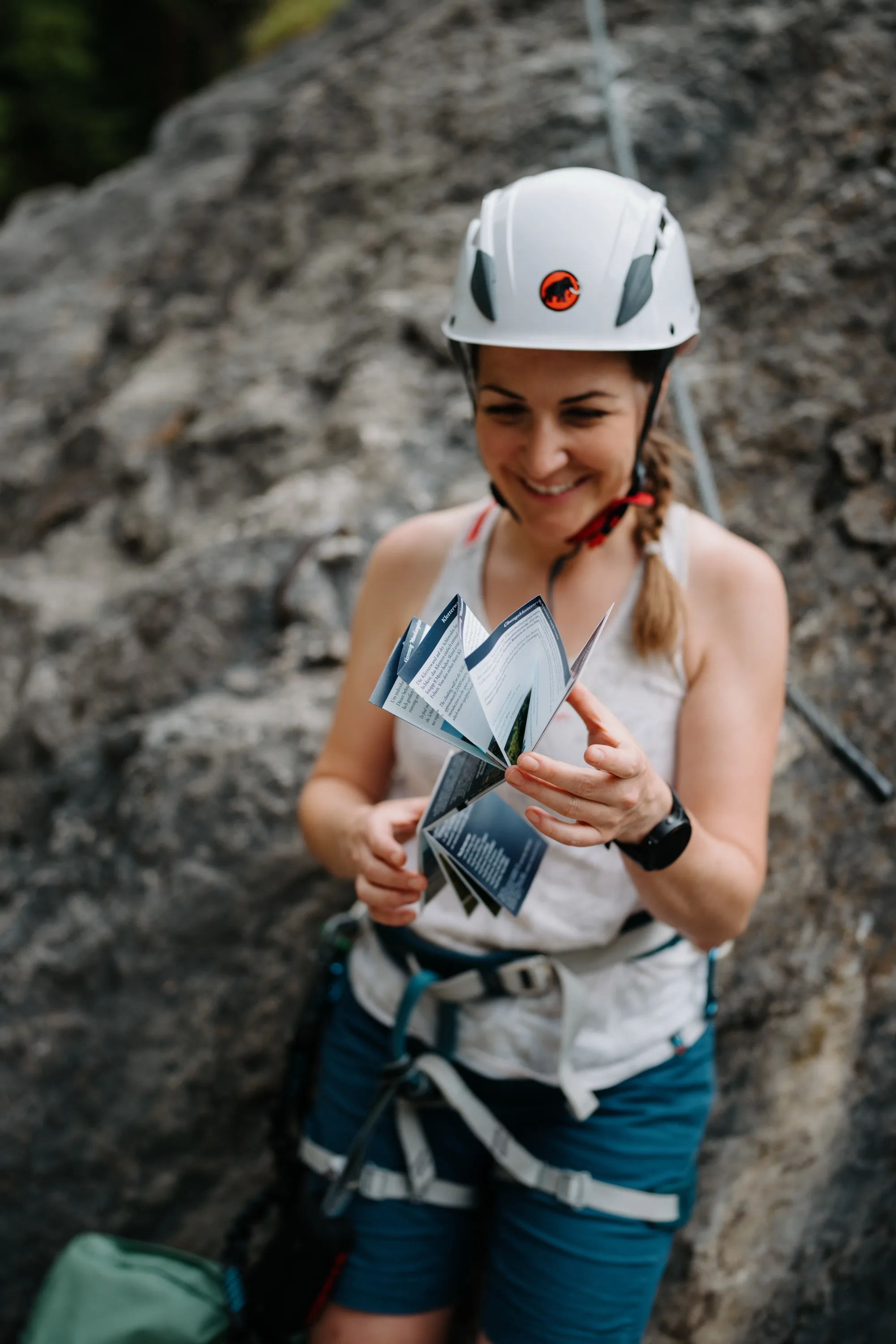 Un'arrampicatrice ripiega la guida per vie ferrate della Gasteinertal – pratica piega a leporello della Twin-Card sulla via ferrata