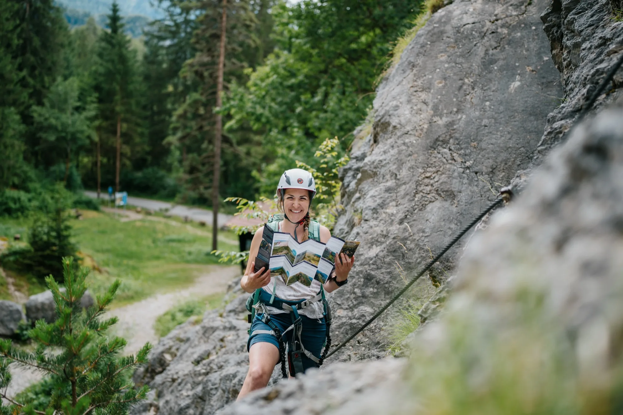 Arrampicatrice mostra una guida alle vie ferrate Gasteinertal aperta su una via ferrata con panorama montano sullo sfondo